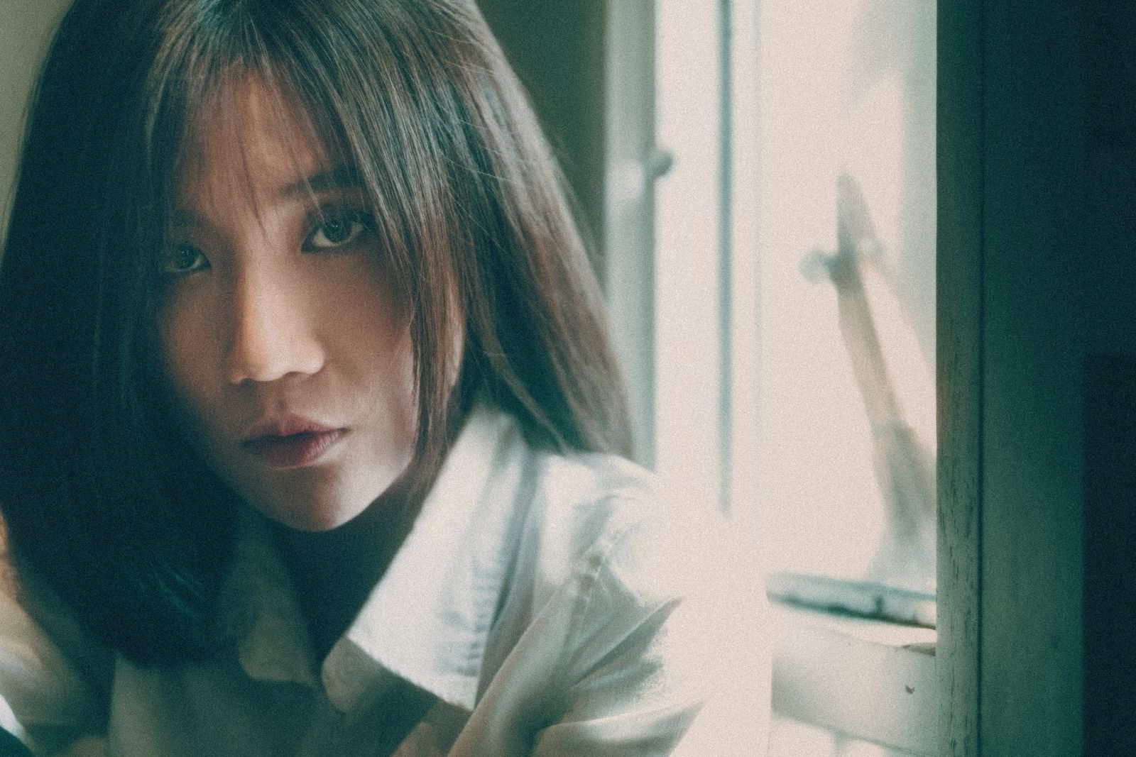 A woman sitting beside a window in soft daylight.