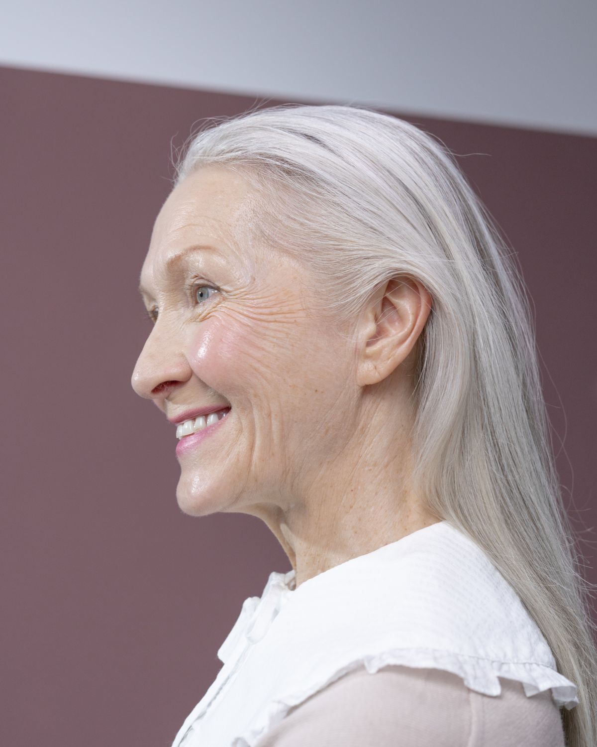 An older woman with long silver hair smiling in profile.