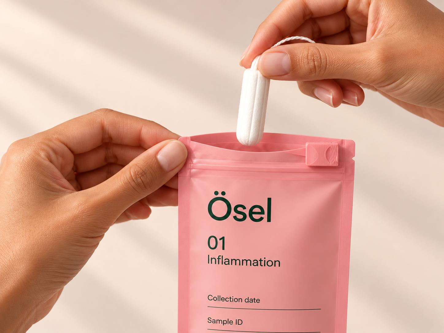 A hand holding a clean white tampon above a matte pink Ösel pouch